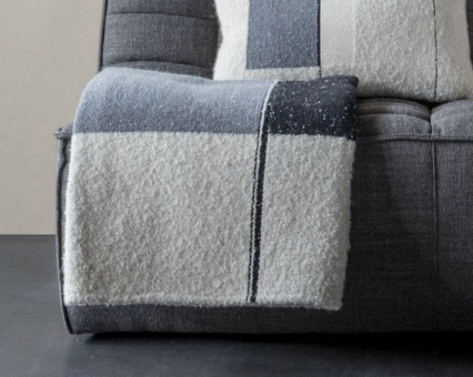 Weiche, grau-weiße Kuscheldecke mit Blockmuster und passendes Zierkissen auf einem grauen Sofa.