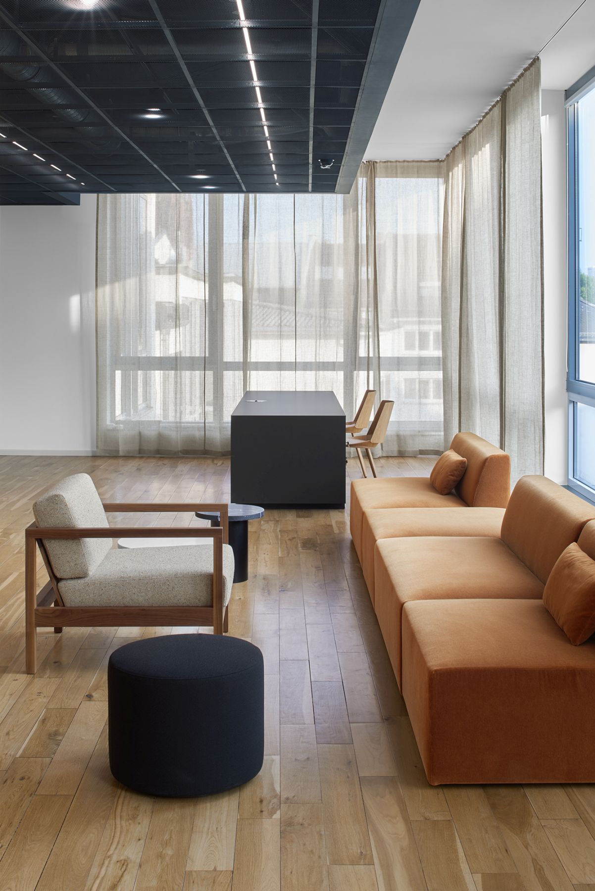 Moderner Büroraum mit e15 Enoki CT09 Beistelltisch in Schwarz, Sessel, Sofa und Holzboden für stilvolles Interieur.