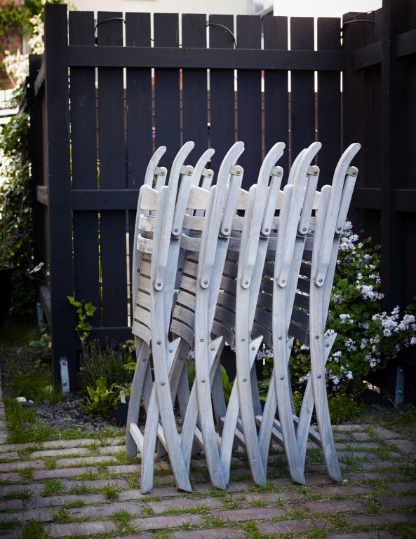 Gestapelte Selandia Armchair Gartenstühle von Skagerak by Fritz Hansen vor einem dunklen Holzzaun im Außenbereich.