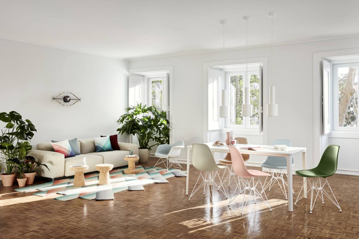 Helles Wohnzimmer mit Vitra Eye Clock Wanduhr, Sofa, Esstisch und bunten Eames Stühlen.