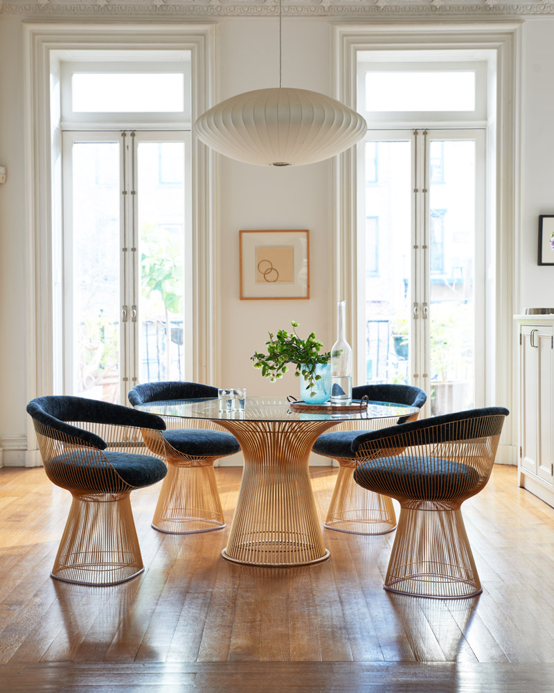 Esszimmer mit Platner Tisch von Knoll International, Glasplatte und goldenem Drahtgestell, umgeben von Stühlen.