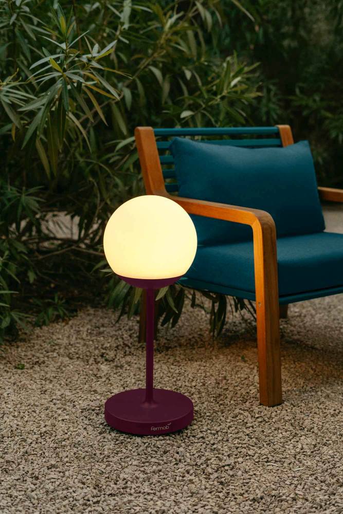 Nahaufnahme des Fermob Somerset Outdoor Sessels mit passender Lampe in Pflaume vor Grün.
