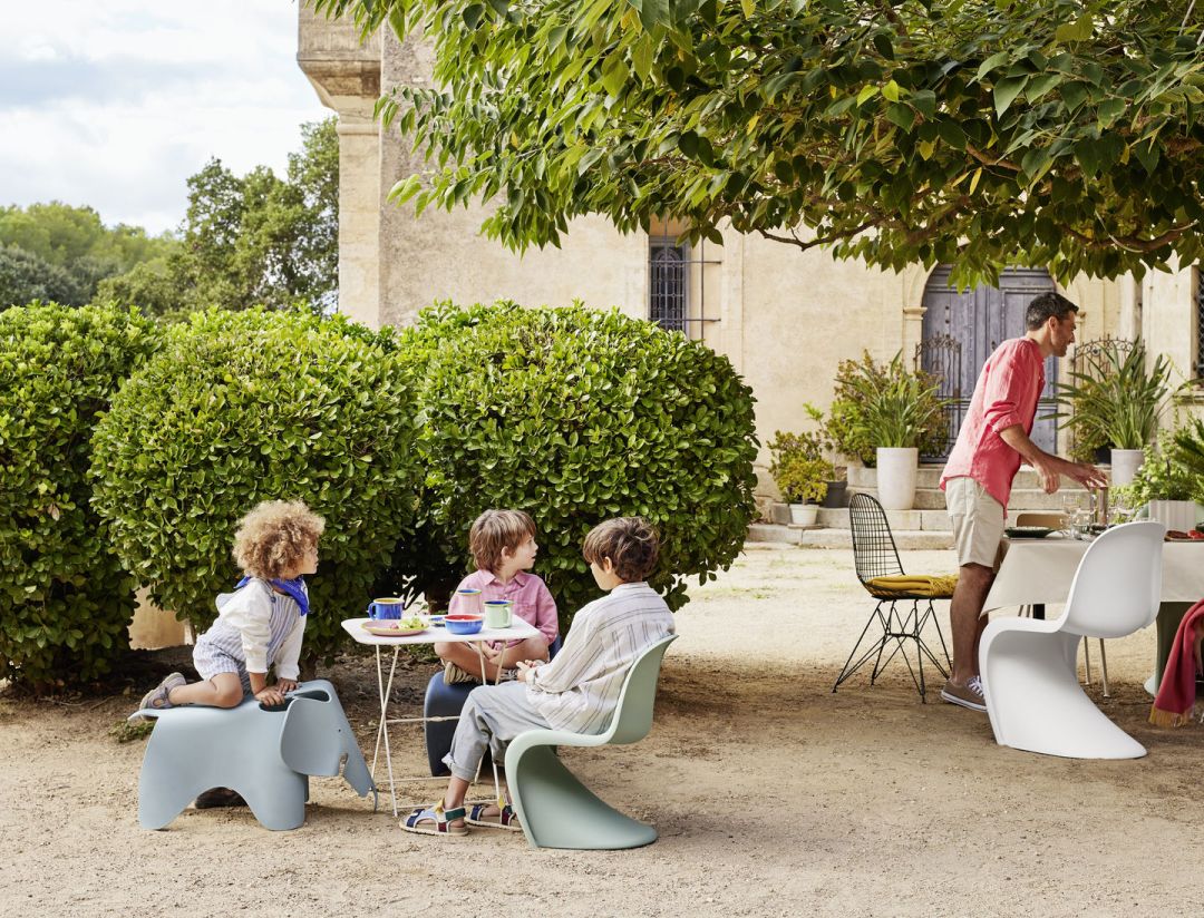 Kinder sitzen an Gartentisch mit Vitra Elephant Hocker und Panton Chair Stühlen.