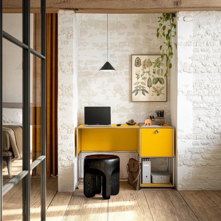 Gelber USM Haller Schreibtisch mit Laptop, Hocker und Accessoires vor einer weißen Backsteinwand.
