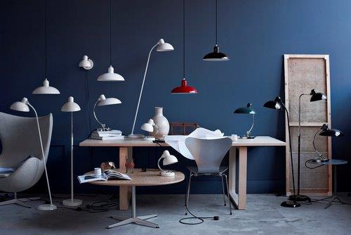 Helles Interieur mit Fritz Hansen Essay Tisch, Stuhl, verschiedenen Lampen und Dekoration vor einer blauen Wand.