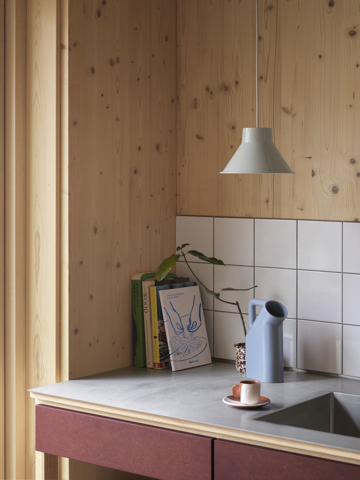 Moderne Küche mit Muuto Top Pendant Pendelleuchte in Dunkelgrün über einer Arbeitsplatte mit Dekoration.