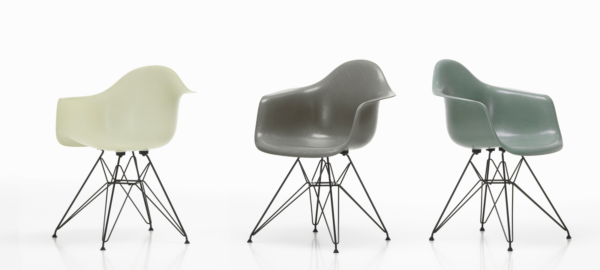 Drei Vitra Eames Fiberglass Arm Chairs DAR Stühle in Weiß, Grau und Grün auf filigranem Metallgestell.
