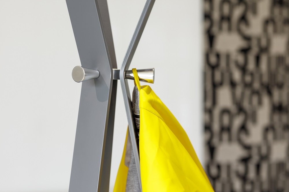 Detailaufnahme einer modernen, grauen Garderobe mit gelber Tasche und silbernen Haken.