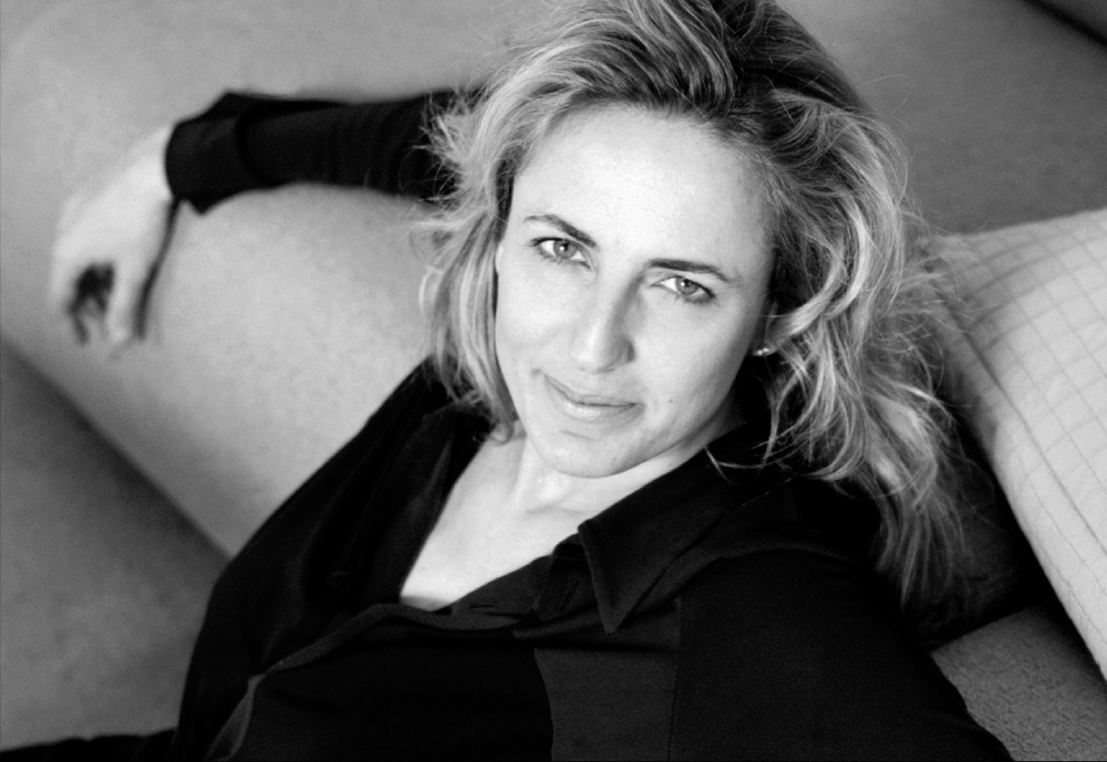 Schwarzweiß-Porträt einer Frau mit blonden Haaren, die eine schwarze Bluse trägt und lächelt.