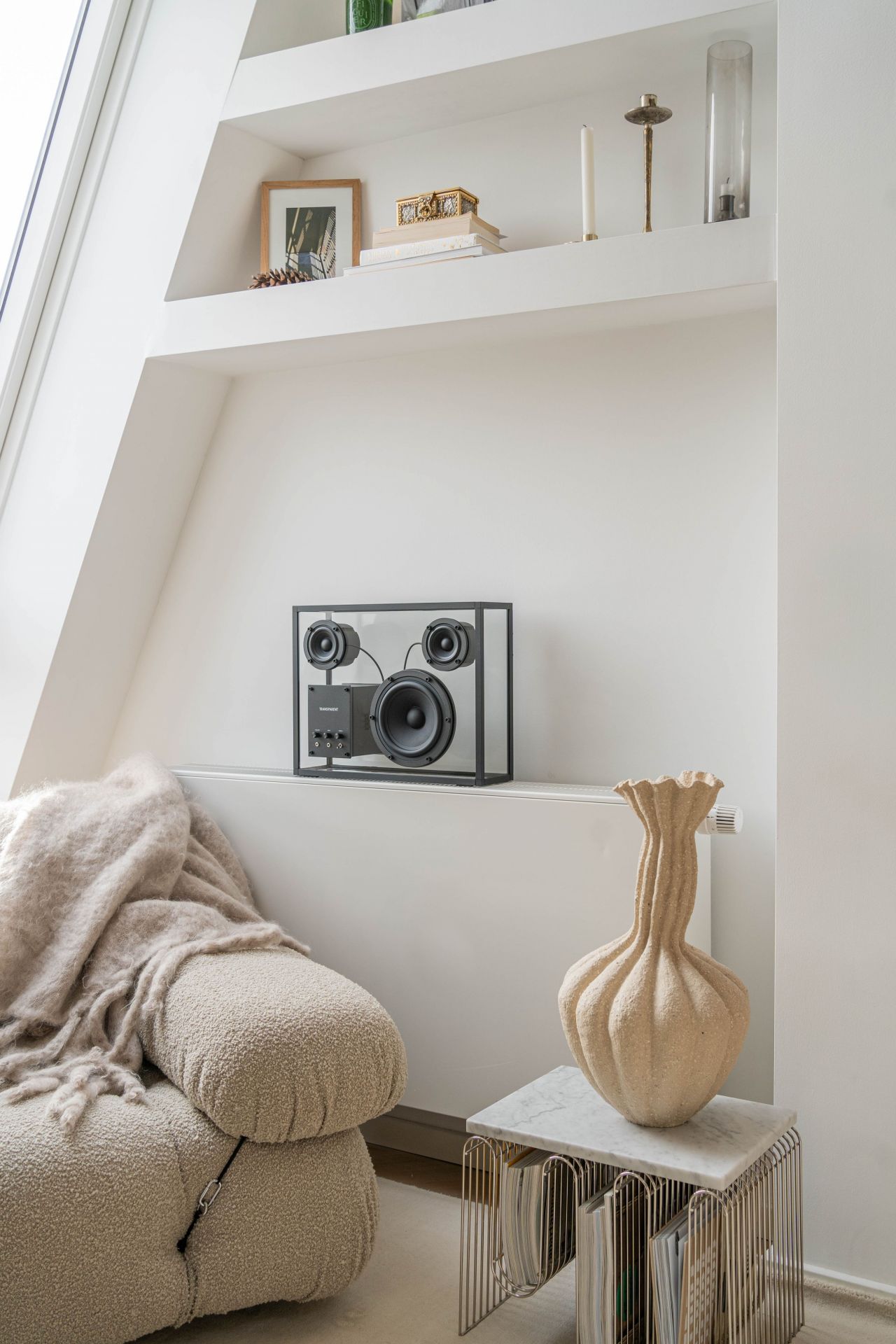 Moderner transparenter Lautsprecher im minimalistischen Wohnzimmer-Interieur mit Sessel und Dekoration. Hochwertige Audioanlage für Musikliebhaber.