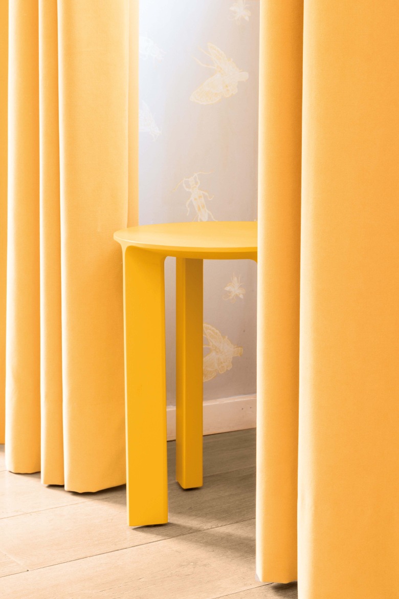 Gelber Hans Hocker von Schönbuch zwischen gelben Vorhängen, minimalistisches Design für moderne Wohnräume.