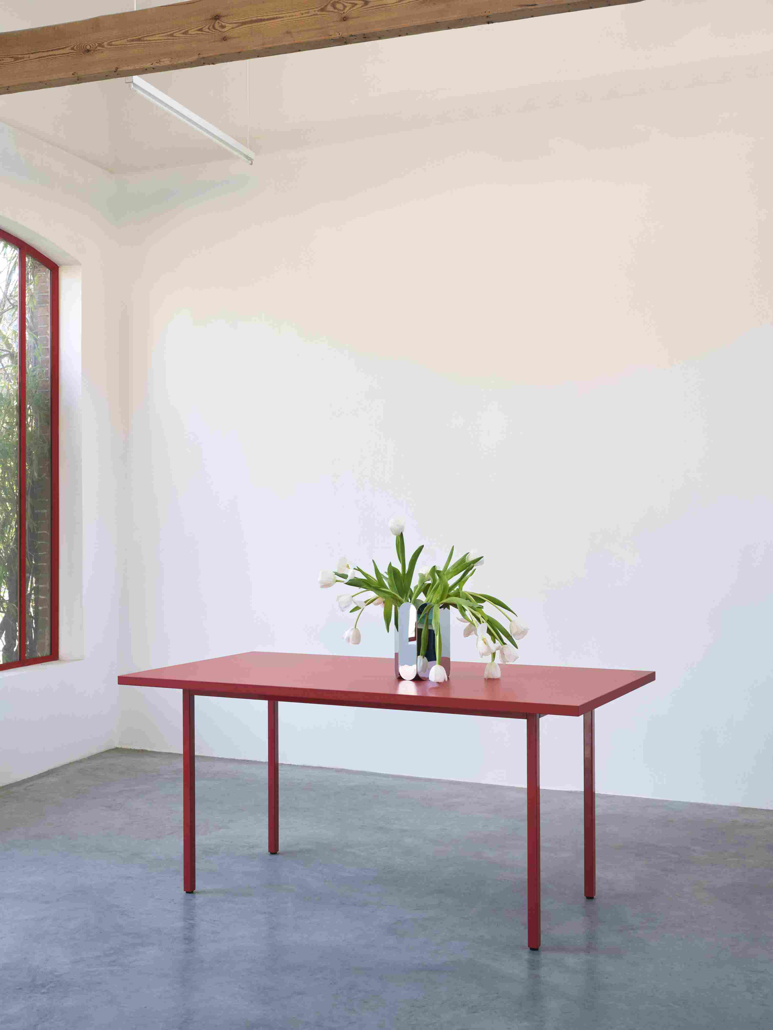 Hay Arcs Vase L Mirror auf rotem Tisch mit weißen Tulpen in minimalistischem Raum.