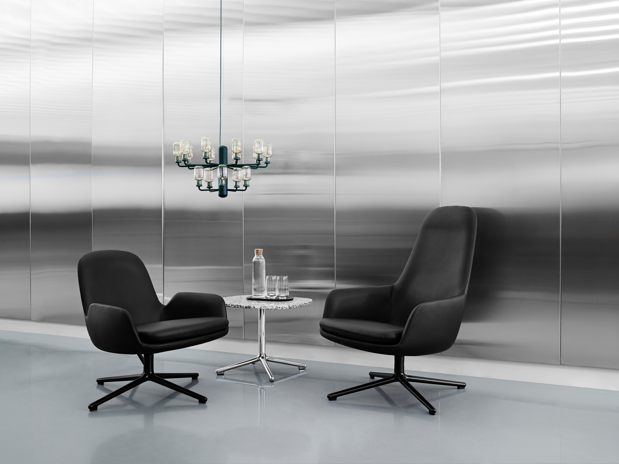 Normann Copenhagen Amp Chandelier Pendelleuchte über schwarzem Sessel-Set mit Marmortisch in modernem Interieur.