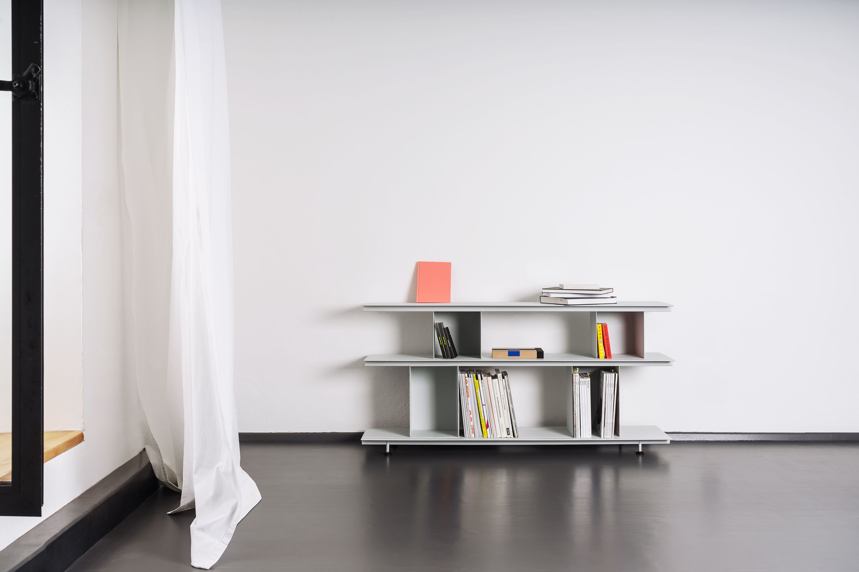 Helles Zimmer mit Zoll D Regal von Nils Holger Moormann, gefüllt mit Büchern und Zeitschriften.