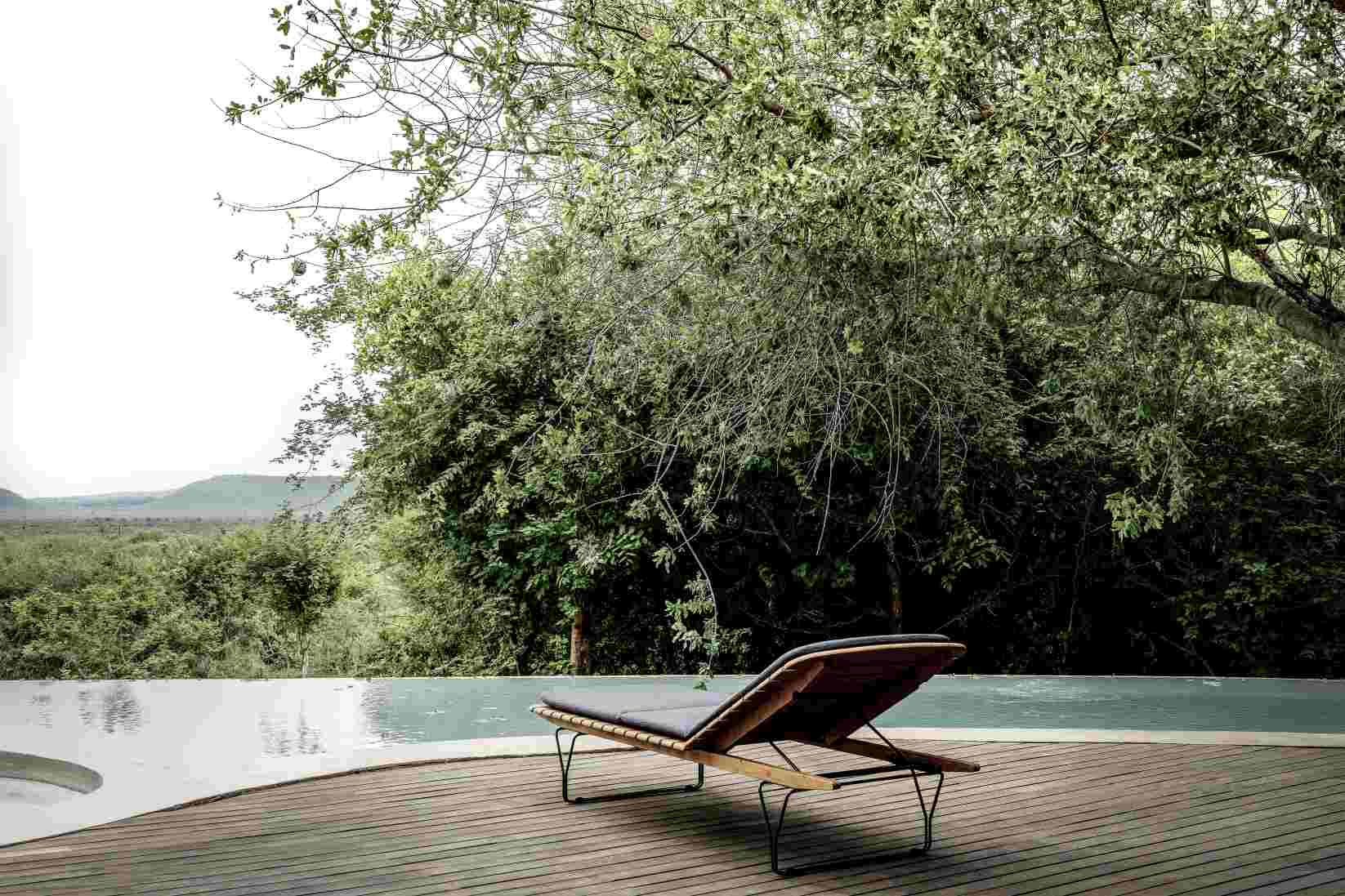 Houe Sonnenliege mit Molo Outdoor Kissen am Pool auf Holzdeck, umgeben von üppigem Grün.