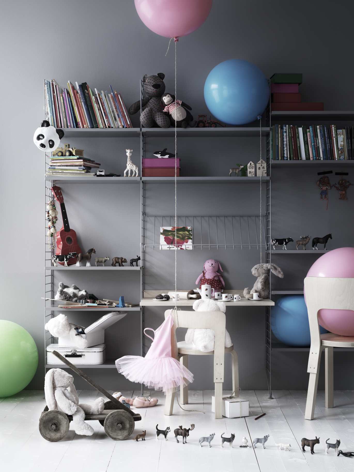 Graues String Regal mit Schreibtisch als Kinderarbeitsplatz, dekoriert mit Spielzeug und Büchern.