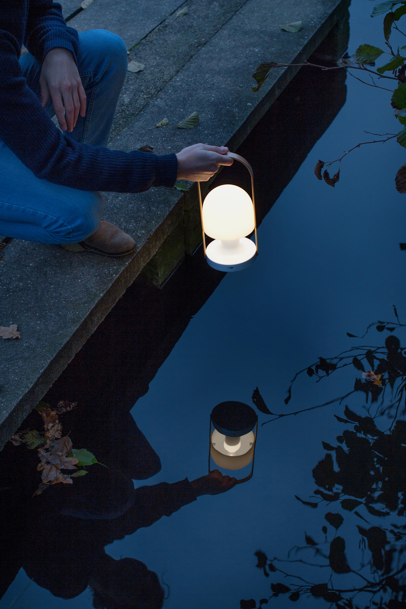 FollowMe LED Akkuleuchte von Marset: Tragbare Tischleuchte mit warmem Lichtschein am Wasser.