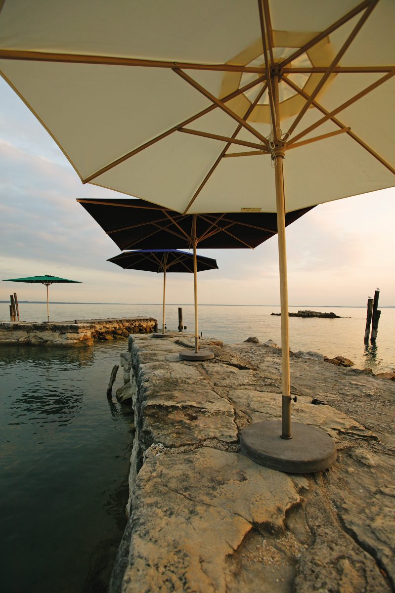 Mehrere Weishäupl Sonnenschirme am Seeufer, klassische Schirme in verschiedenen Farben für den Garten.