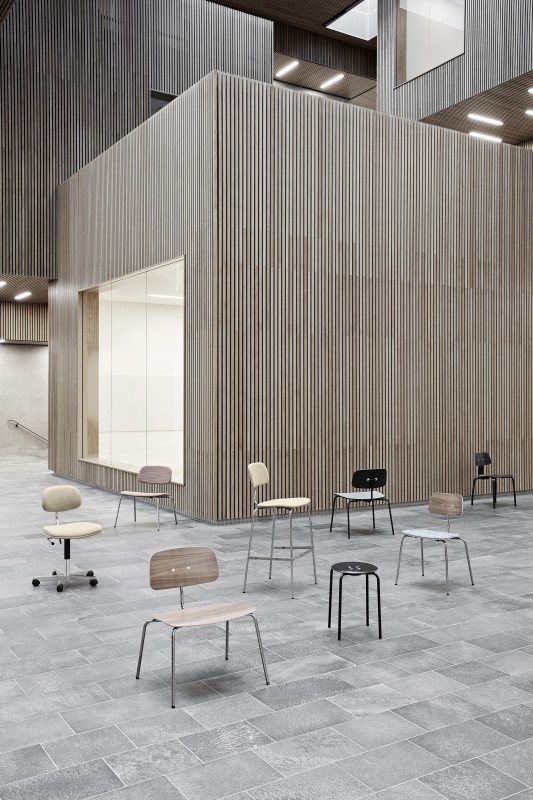 Kevi Stuhl Kollektion: Bürostuhl, Barhocker und Holzstühle in verschiedenen Ausführungen vor einer Holzwand.