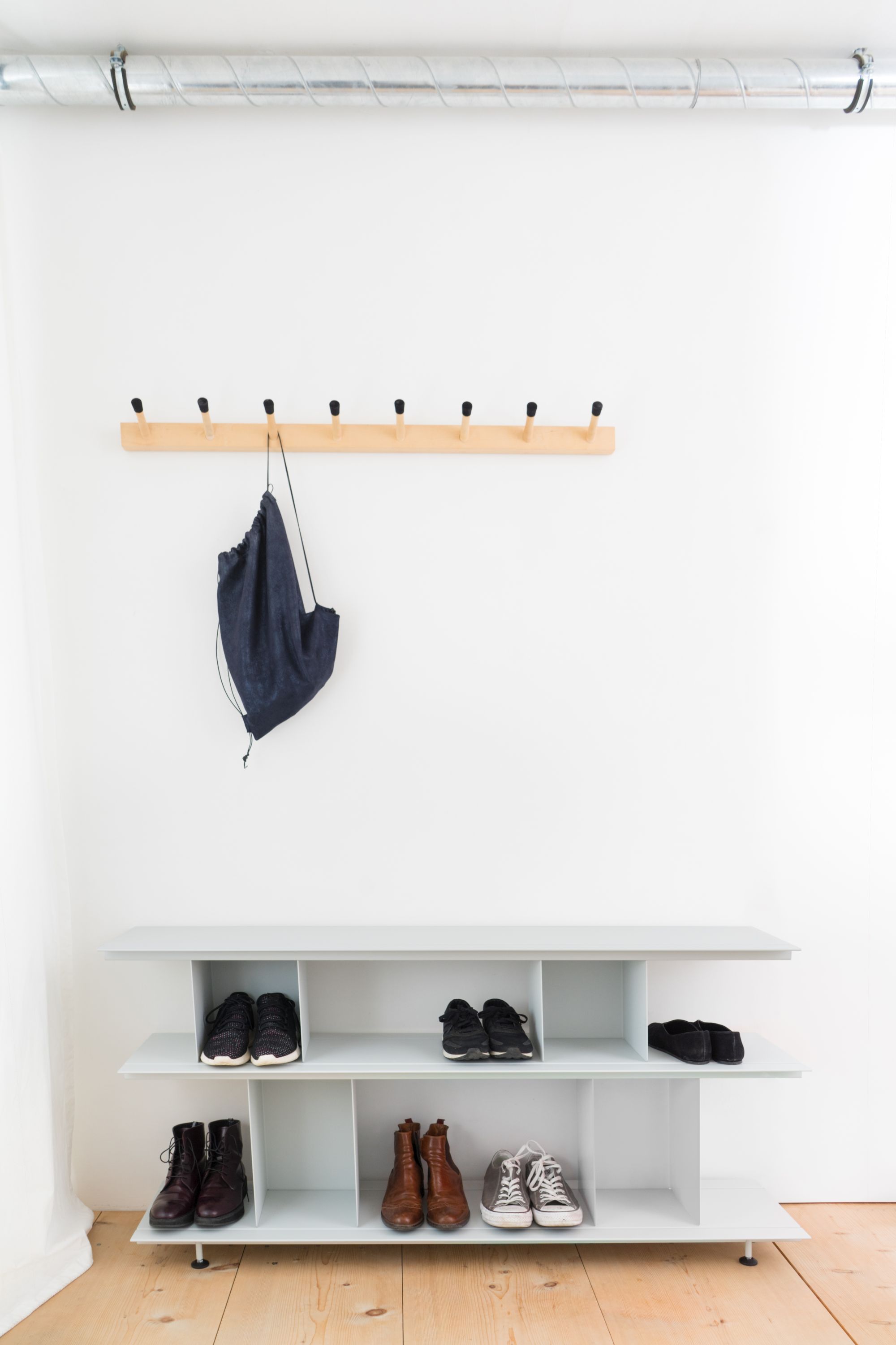 Helles Entree mit Moormann Zoll D Regal, Holzgarderobe, Schuhen und Stoffbeutel vor weißer Wand.