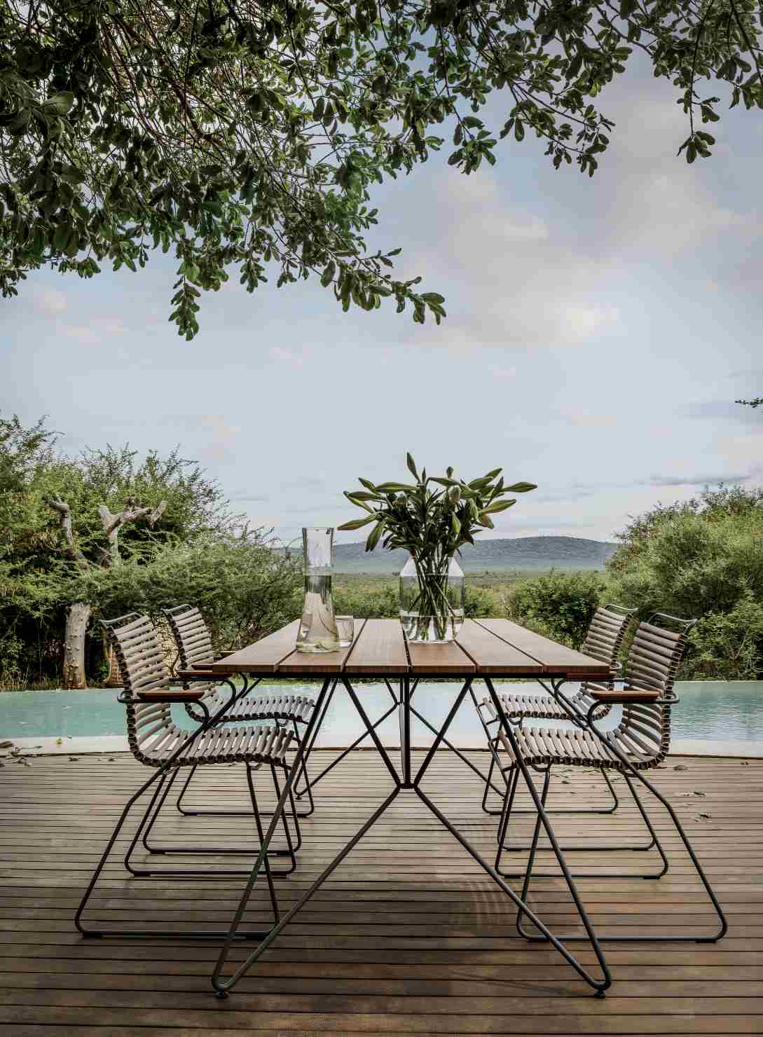 Houe Click Dining Stuhl mit Armlehne, schwarzes Gestell, am Esstisch im Garten.