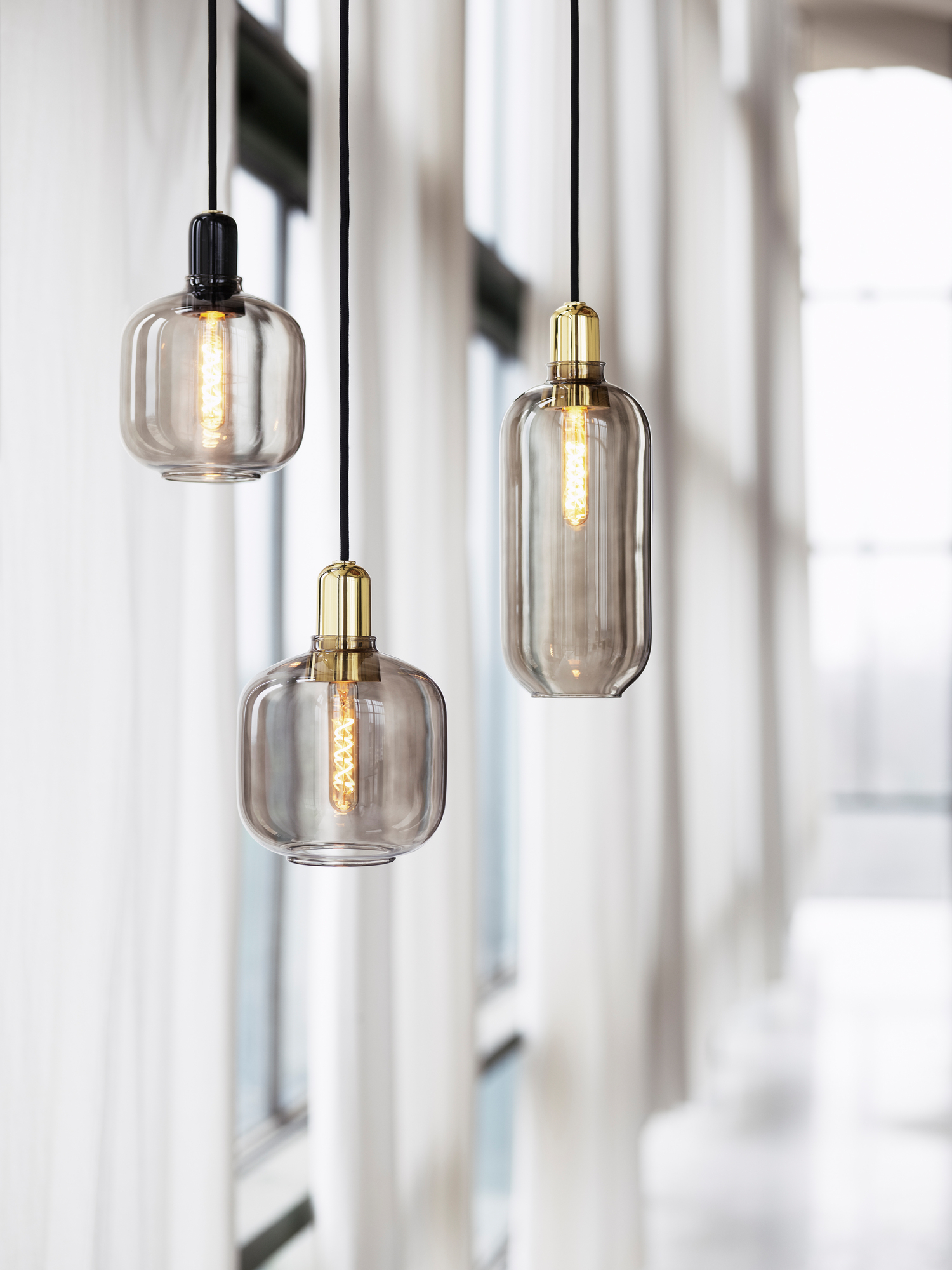 Drei gold-grüne Amp Lamp Pendelleuchten von Normann Copenhagen vor hellem Hintergrund.