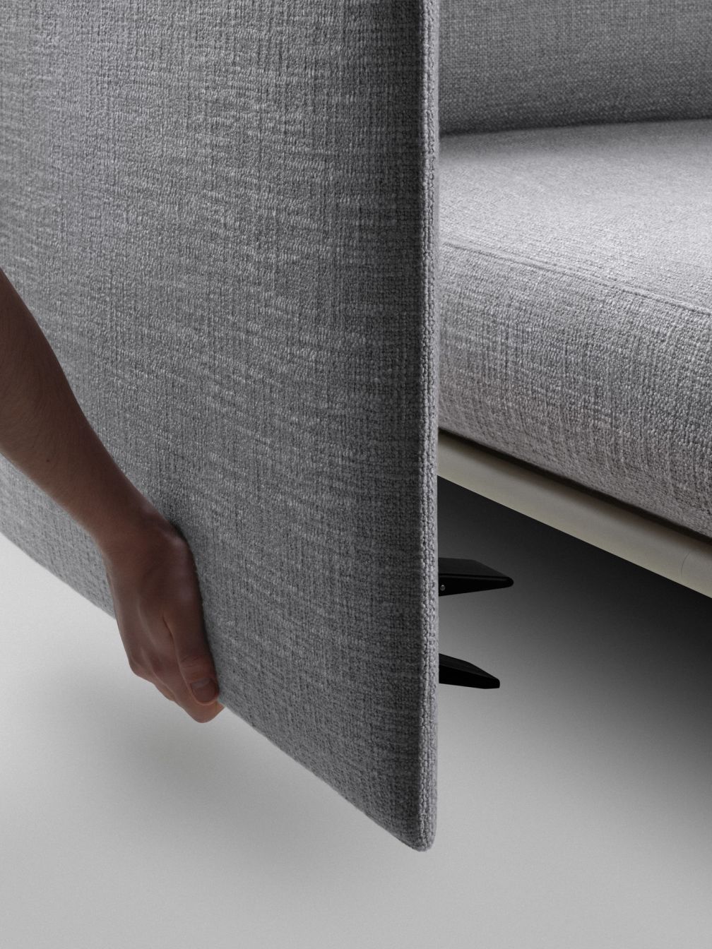 Detailaufnahme: Hand öffnet graues Stoffpaneel eines modularen Sofas mit Stauraum.