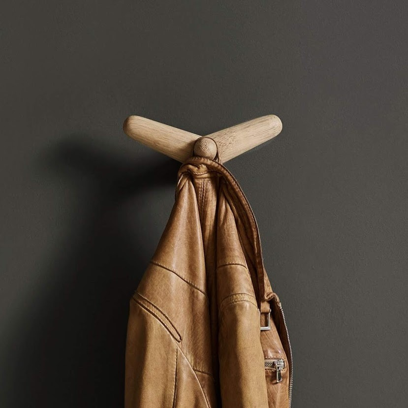 Tail Wing Haken von Woud, ein minimalistischer Garderobenhaken aus hellem Holz mit brauner Lederjacke.