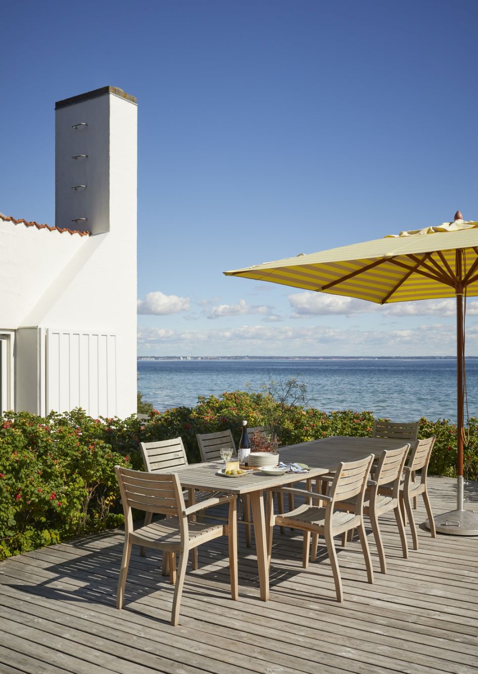 Ballare Chair Stuhl von Skagerak by Fritz Hansen, Outdoor-Esstisch mit Stühlen und Sonnenschirm auf Holzterrasse am Meer.