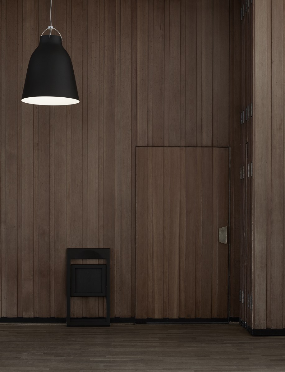 Schwarze Caravaggio Pendelleuchte von Fritz Hansen vor einer Holzwand, minimalistisches Design, Innenbeleuchtung.