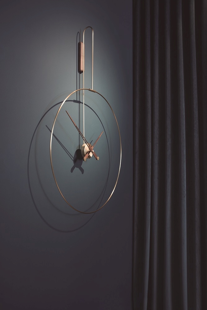 Daro Clock Wanduhr: Moderne, goldene Wanduhr mit Holzdetails an einer dunkelblauen Wand.
