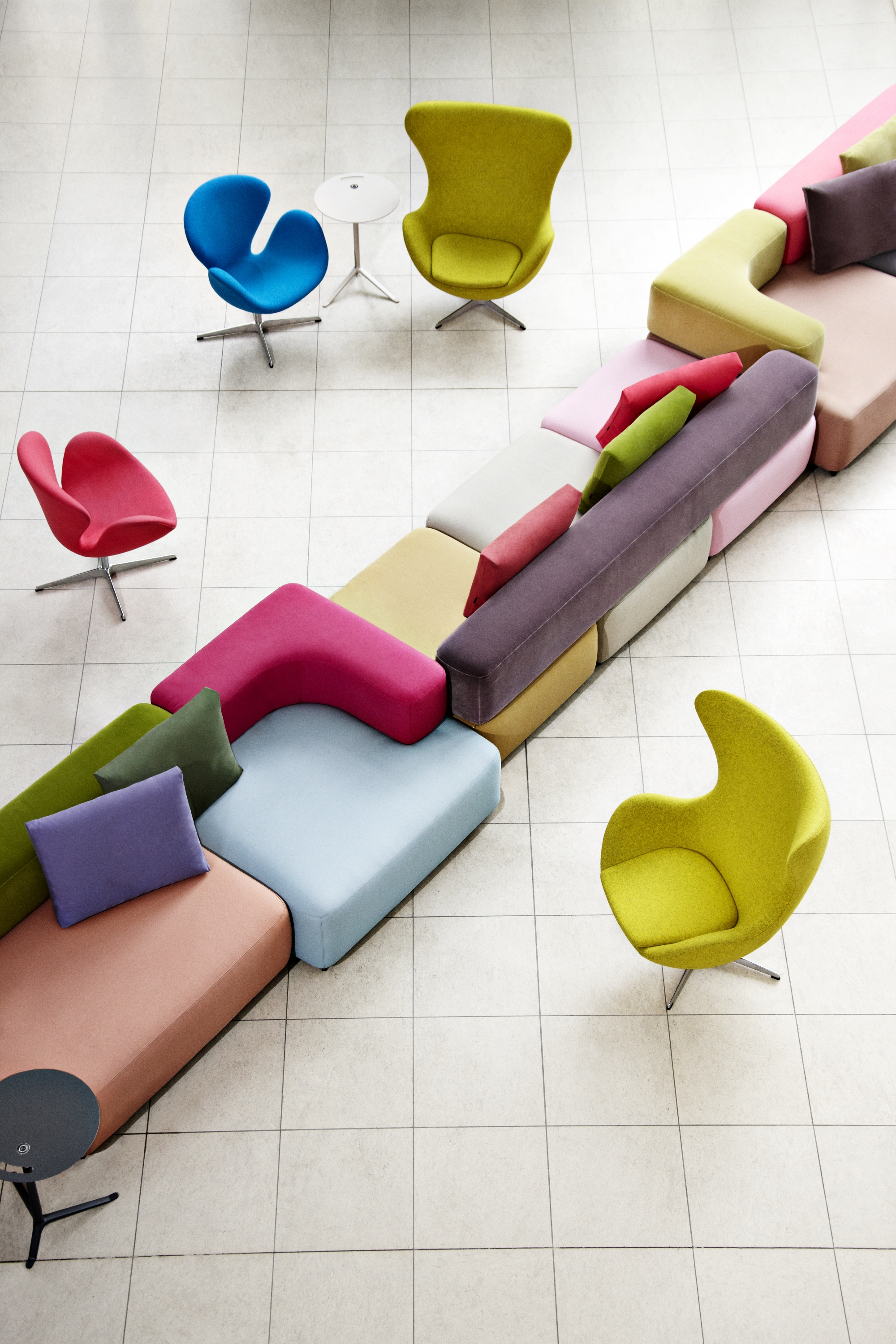 Ansicht von oben: Mehrere farbige Swan Sessel von Fritz Hansen und modulare Sitzmöbel auf hellem Fliesenboden.