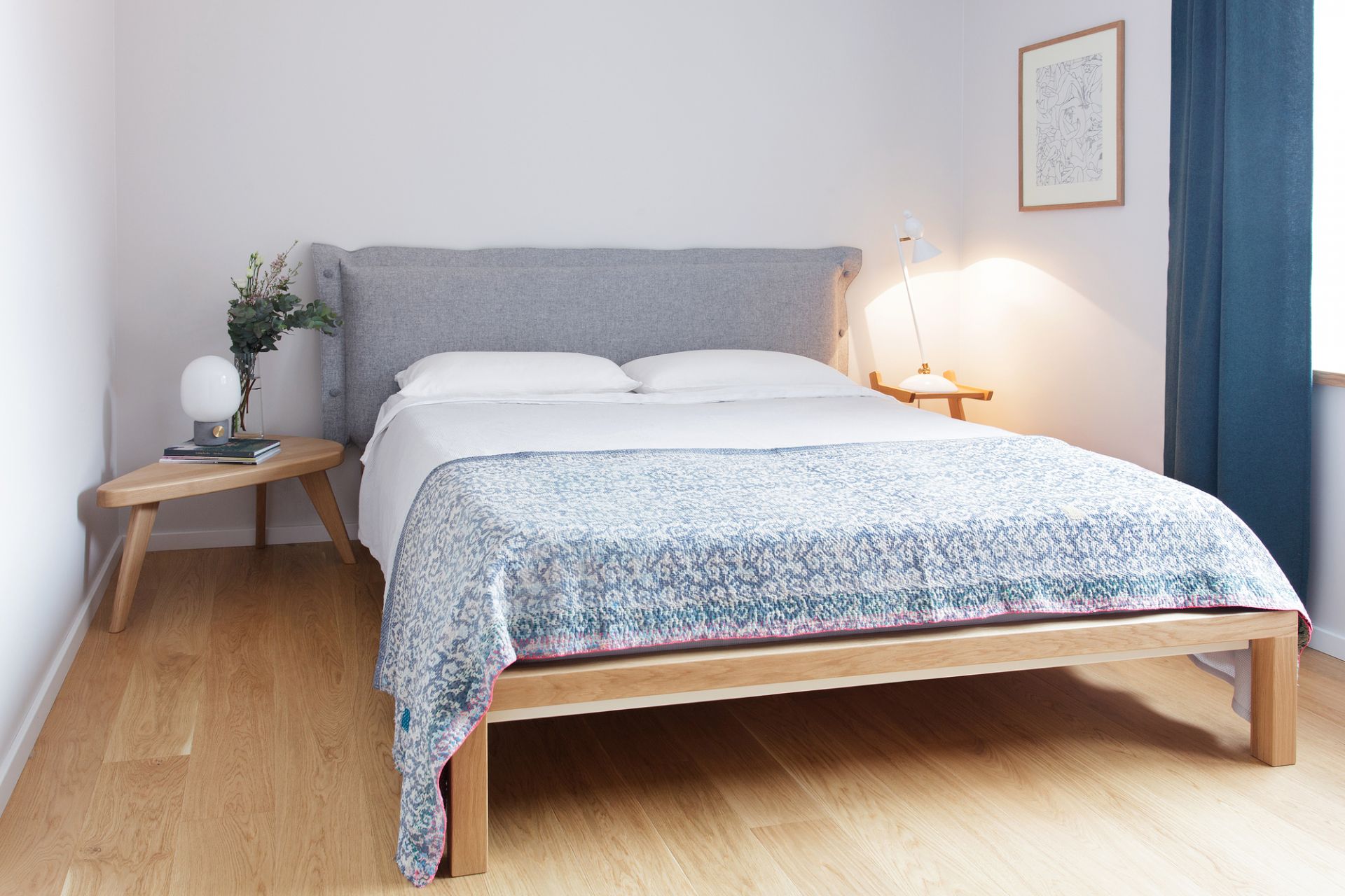 Helles Schlafzimmer mit modernem Holzbett, grauem Kopfteil und blauer Tagesdecke für stilvolles Wohnen.