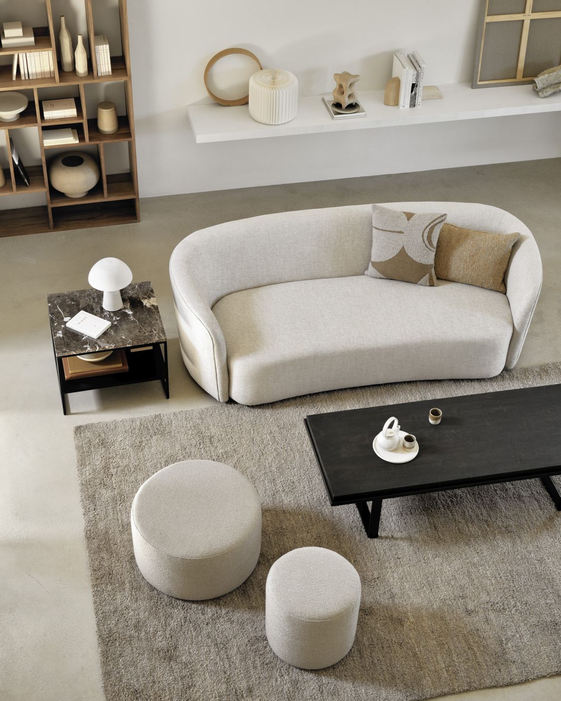 Zwei Ethnicraft Barrow Sitzhocker in hellem Beige vor Sofa und Couchtisch auf Teppich.