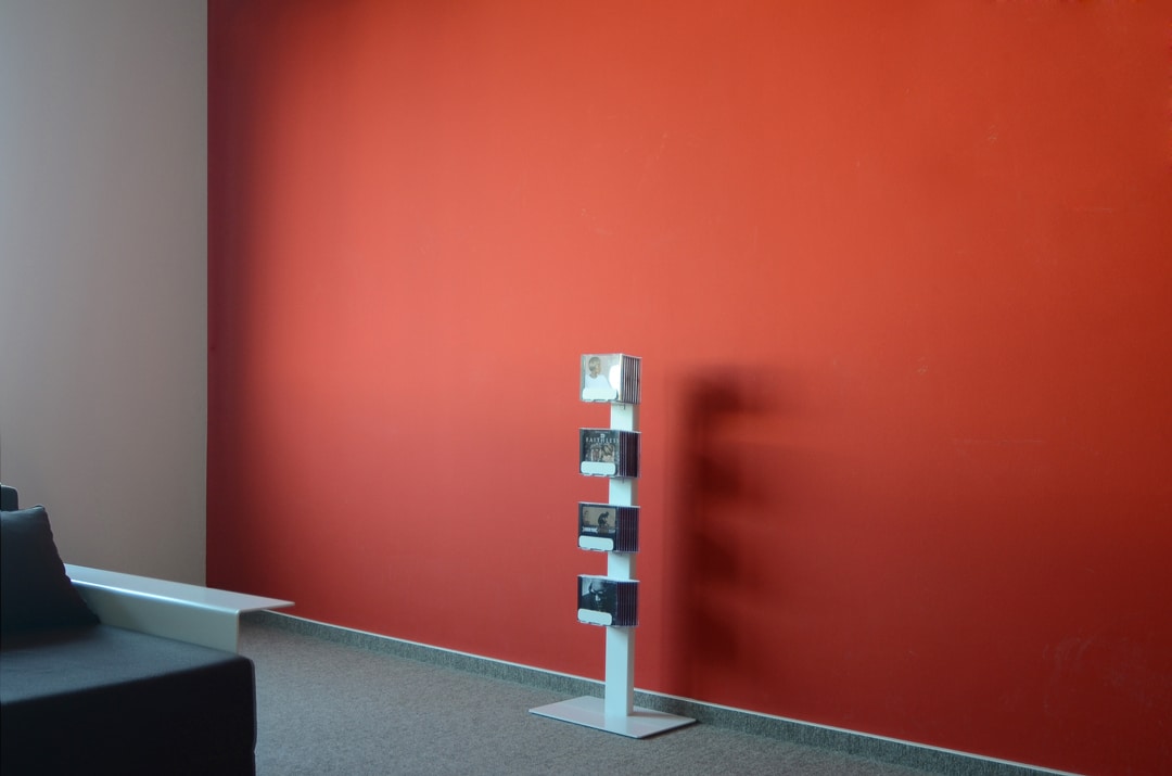Freistehendes, weißes CD-Regal (CD-Baum) mit CDs vor einer roten Wand. Einzeln stehendes Standregal.