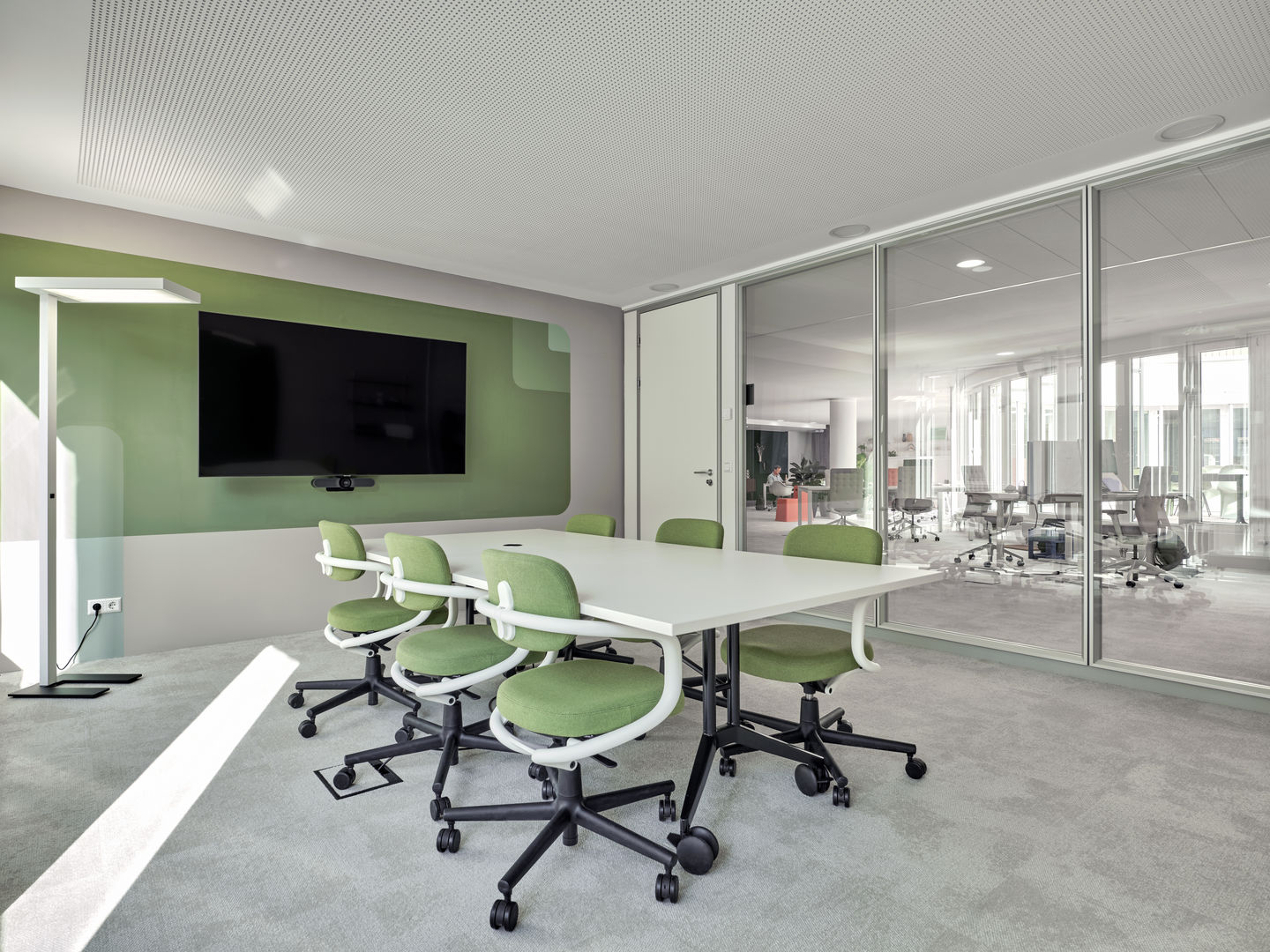 Besprechungsraum mit Vitra MedaMorph Klapptisch, weißen Tischplatte, grünen Stühlen und großem Bildschirm an der Wand.