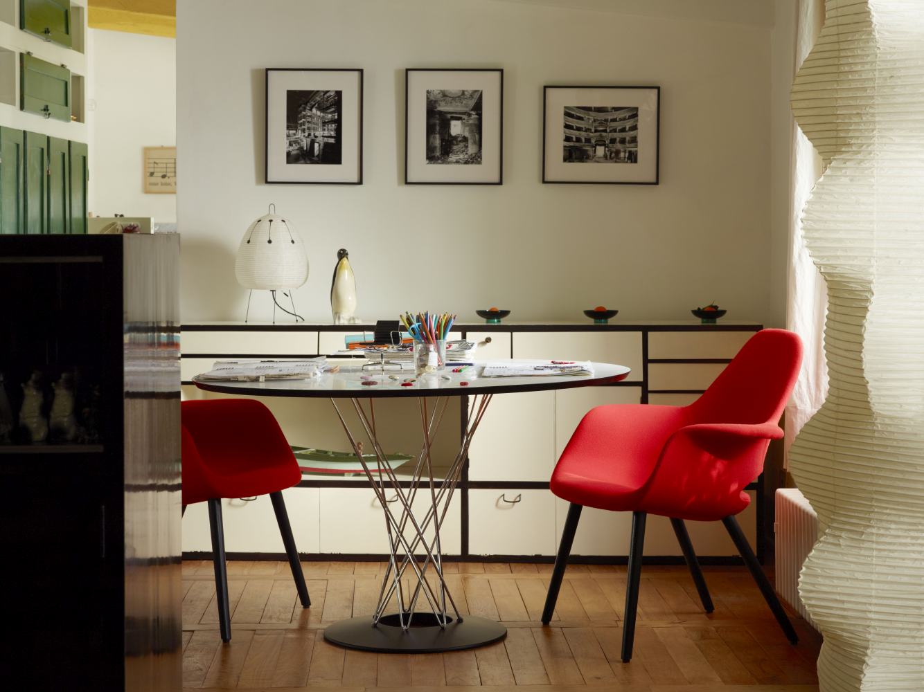 Noguchi Dining Table von Vitra mit Glasplatte und verchromtem Drahtgestell, umgeben von roten Stühlen.
