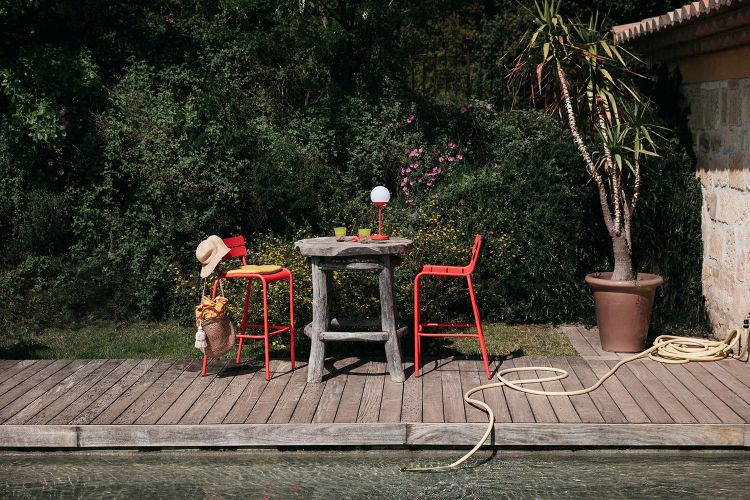 Roter Fermob Luxembourg Barhocker Outdoor mit Tisch und Dekoration auf einer Holzterrasse am Pool.
