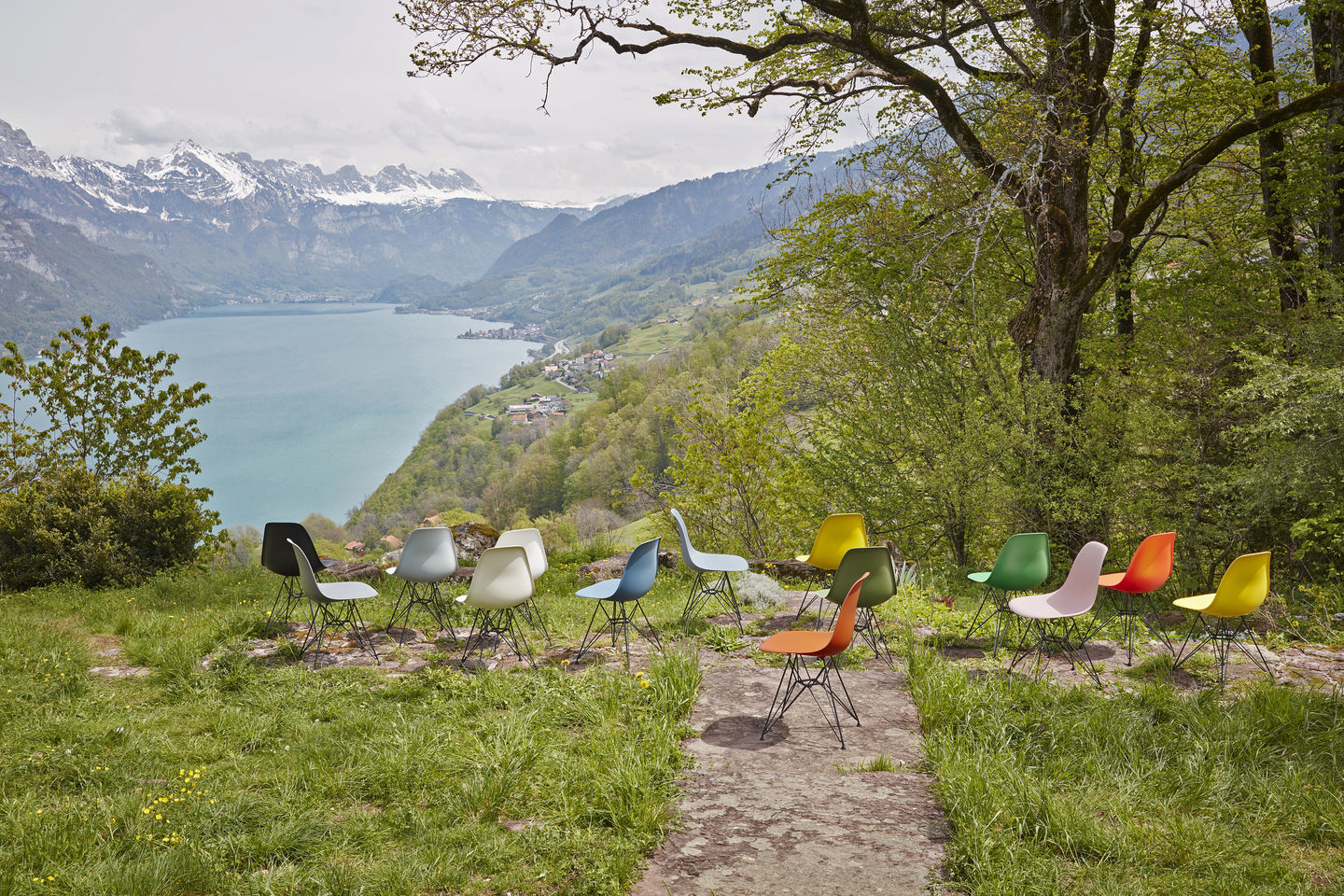 Eine Gruppe von Eames Plastic Arm Chairs DAR Stühlen von Vitra in verschiedenen Farben vor Bergpanorama.