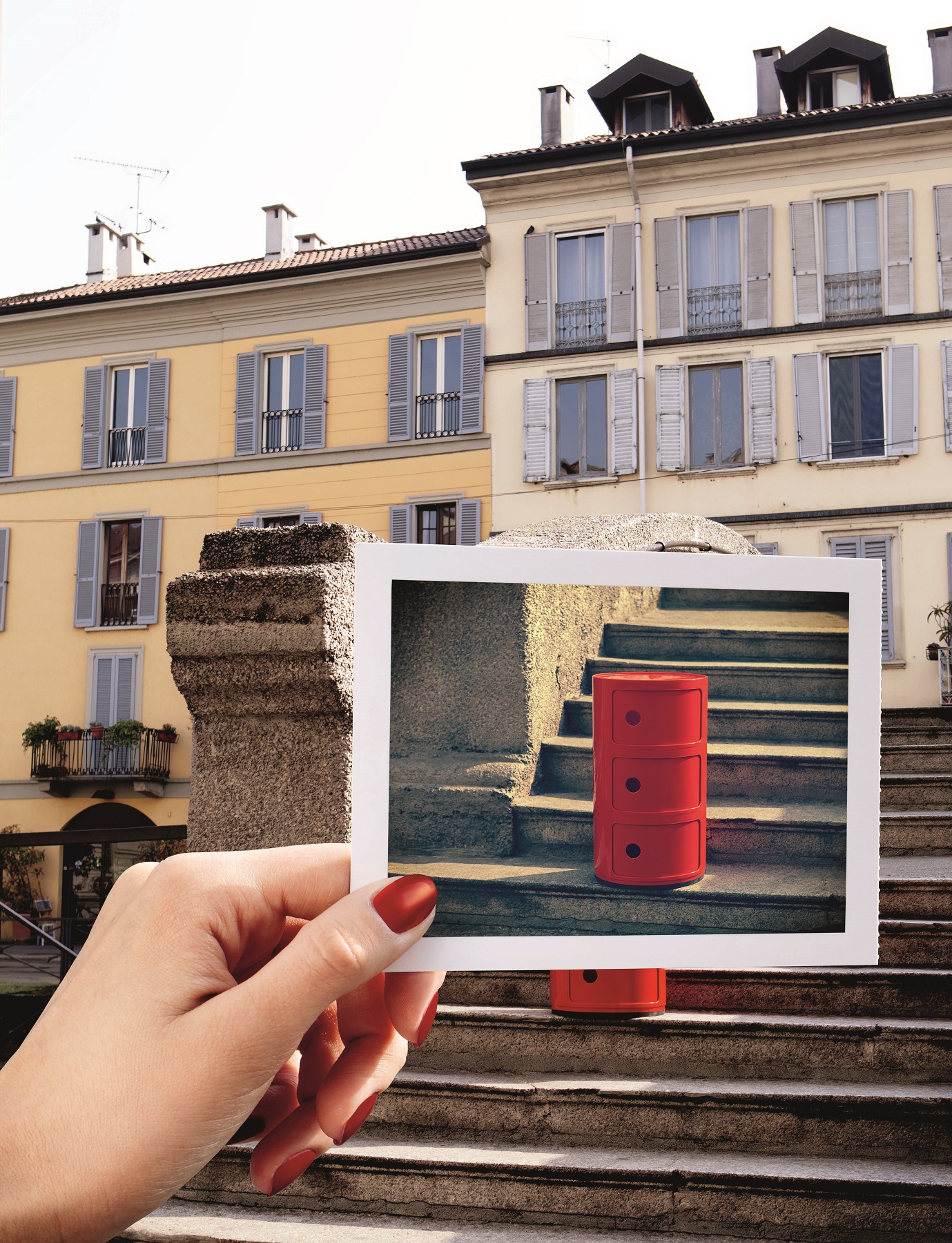 Roter Kartell Componibili Container mit drei Elementen auf einem Foto, gehalten vor italienischer Architektur.