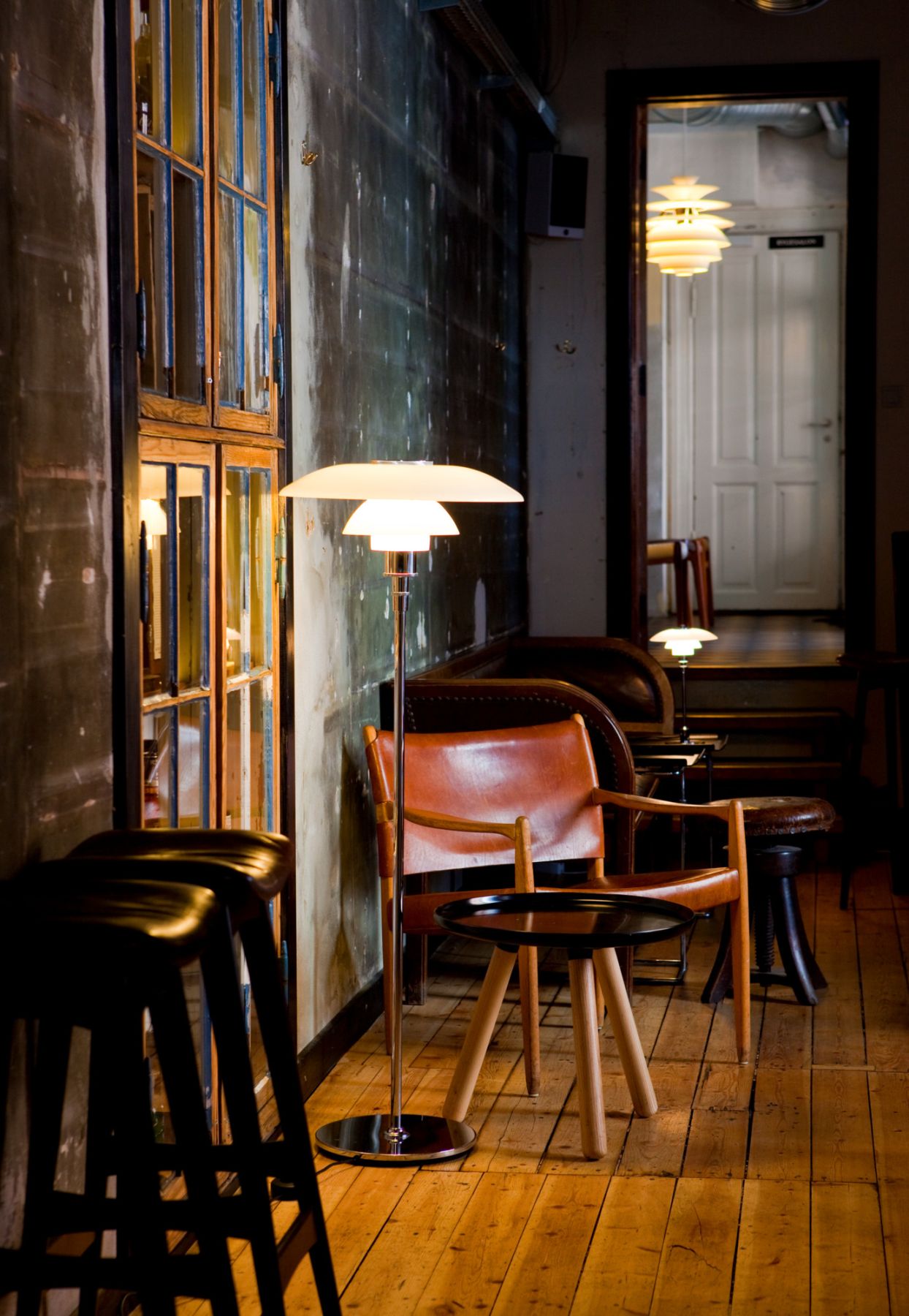 Stehleuchte im dänischen Design neben Ledersessel und kleinem Beistelltisch auf Holzboden in Bar.