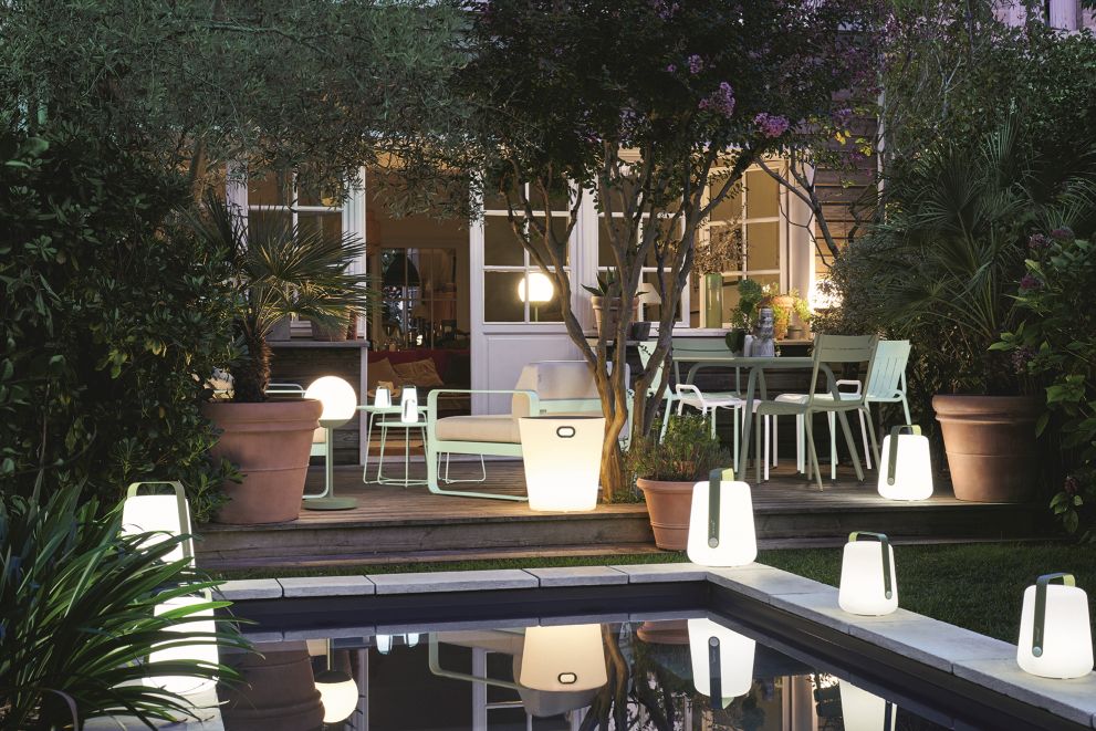 Gartenambiente mit verschiedenen kabellosen LED-Leuchten und Gartenmöbeln, die sich im Pool spiegeln.