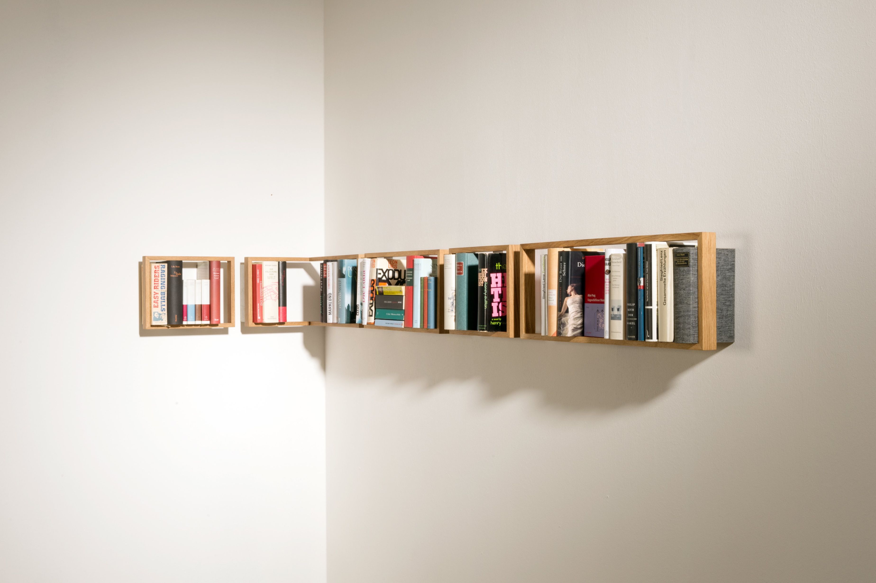 Modernes Bücherregal "b-eck" aus Eiche, kleine Ausführung, an einer weißen Wand mit Büchern gefüllt.