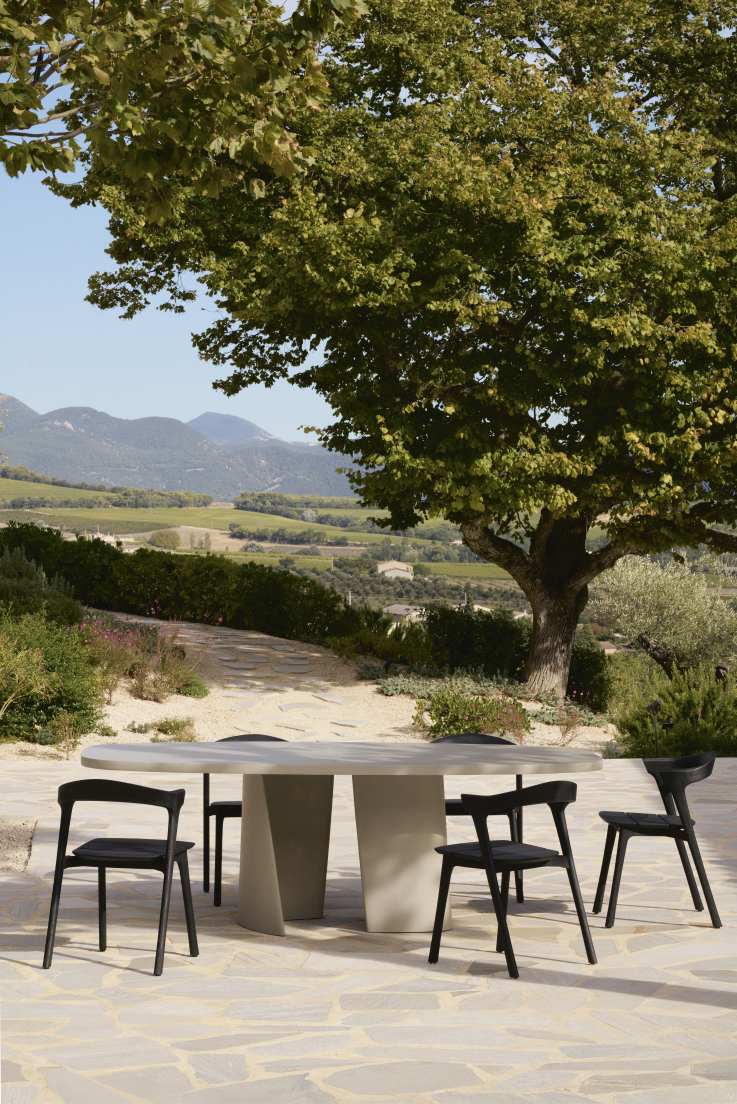 Canyon Outdoor Esstisch von Ethnicraft mit schwarzen Stühlen im Garten mit Blick auf die Landschaft.