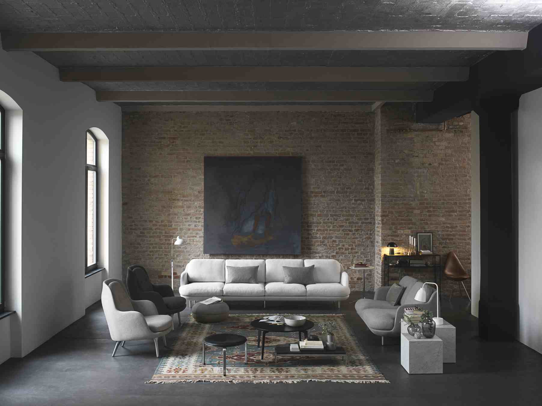 Helles Wohnzimmer mit Fritz Hansen Lune Sofa, Sesseln und Teppich vor einer Backsteinwand.