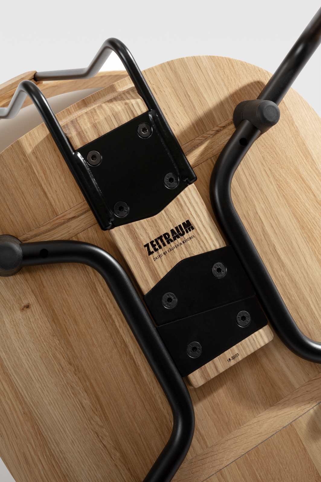 Detailaufnahme der Unterseite des Okito Stuhls von Zeitraum mit schwarzem Metallgestell und Holzstruktur.