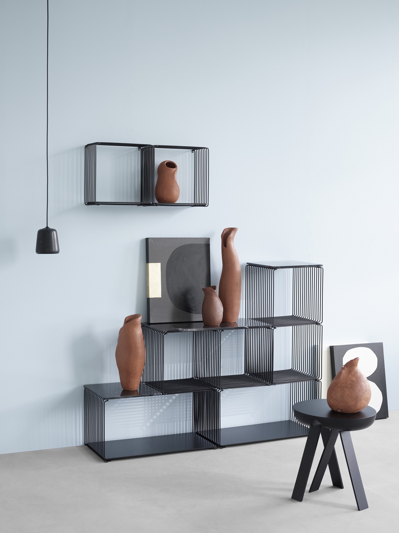 Panton Wire Regalsystem: Schwarze Drahtwürfel als modulares Regal mit Deko-Objekten vor hellblauer Wand.