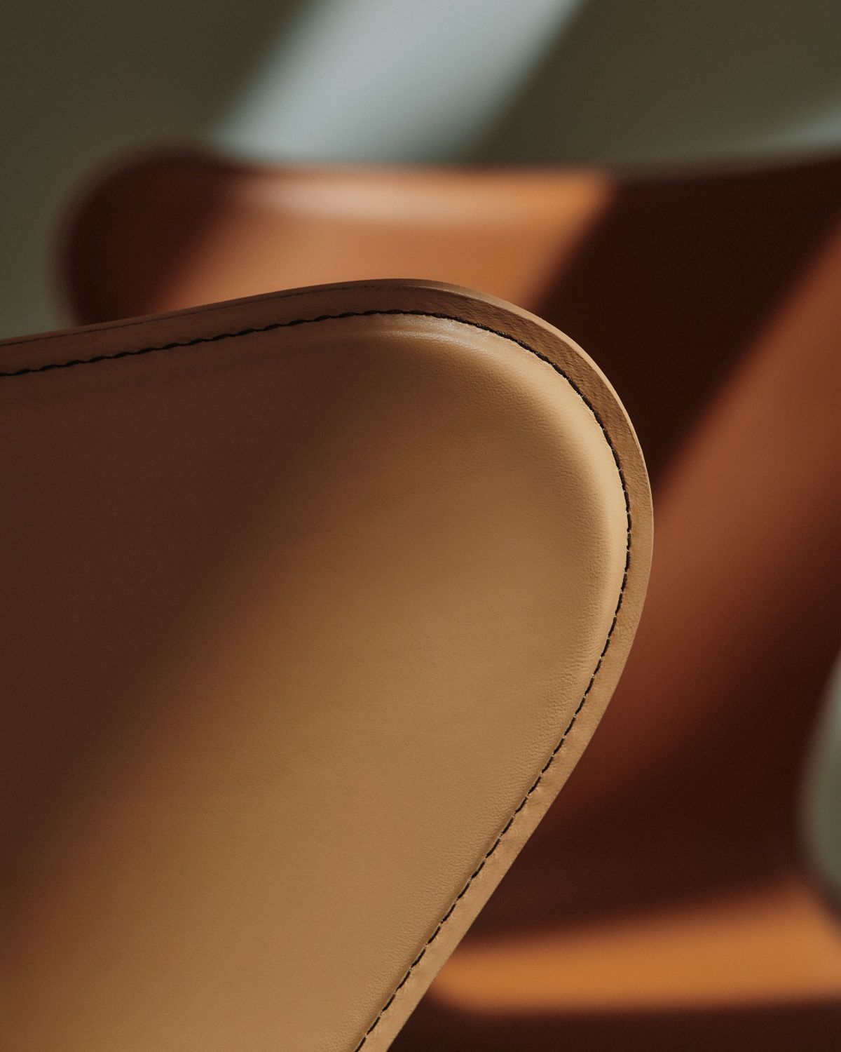 Detailaufnahme eines Siebener Stuhls von Fritz Hansen, Serie 3107, mit braunem Lederbezug und feinen Ziernähten.