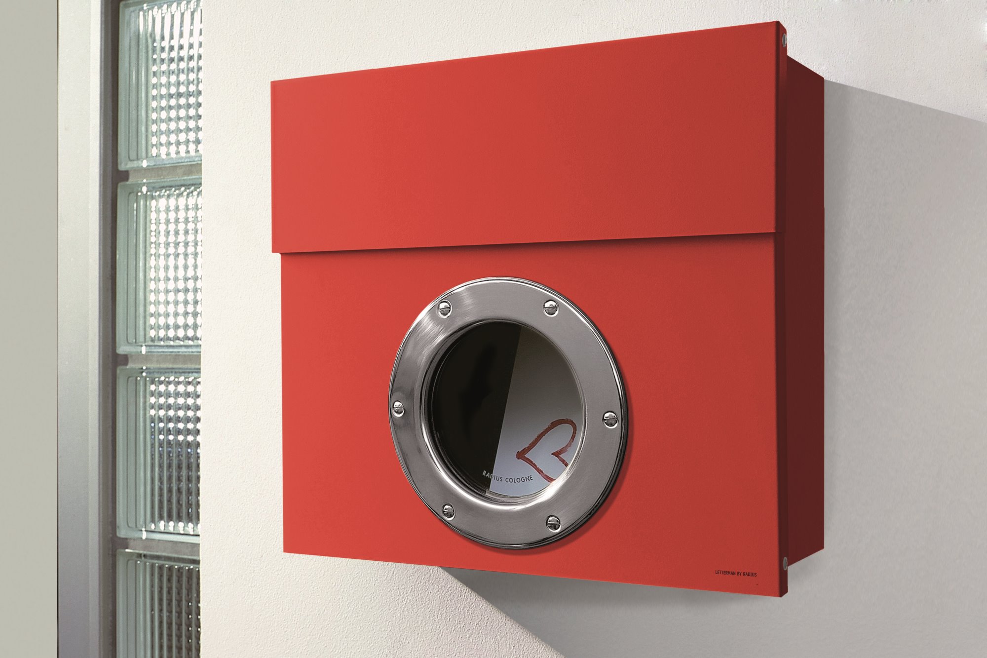 Roter Letterman I Briefkasten von Radius mit Bullauge an einer weißen Wand montiert.