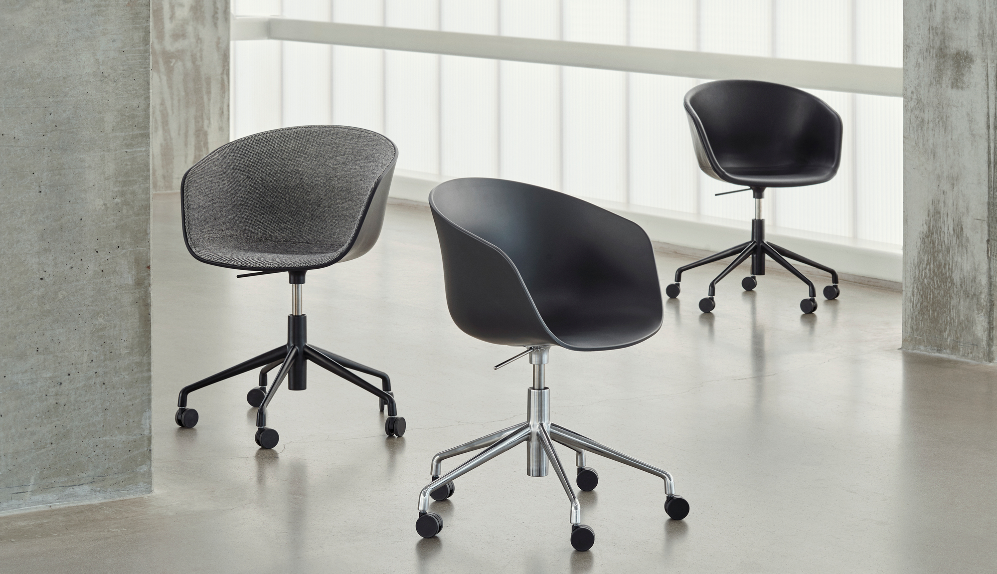Drei Hay About A Chair AAC25 Bürostühle mit Rollen und Vollpolsterung in Grau und Schwarz.